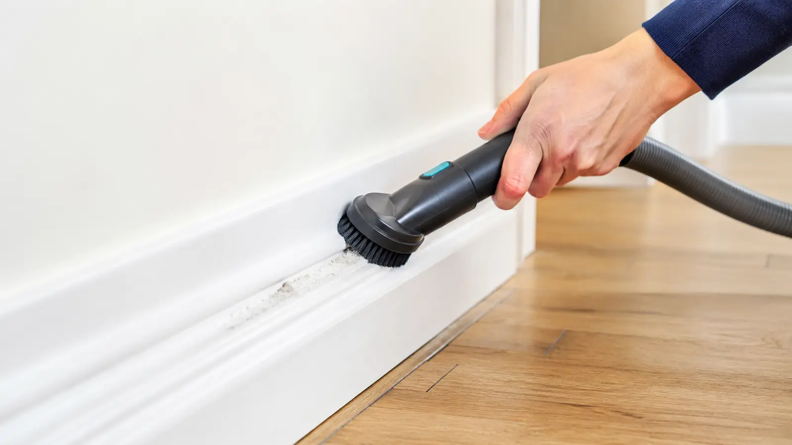 Vacuum brush attachment removing loose dust from a white baseboard